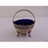 A silver circular bonbon dish with swing handle on four pad feet to include blue glass liner,