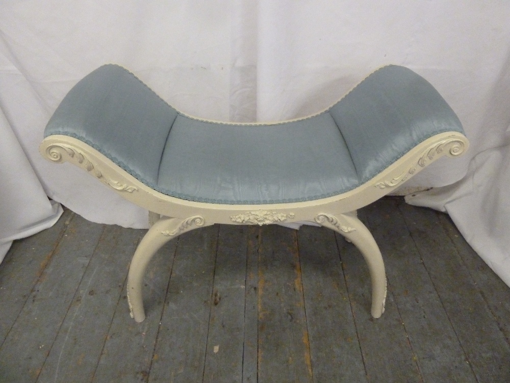 A curved white painted upholstered boudoir stool on sabre legs