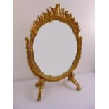 An oval gilded wood heavily carved tilt top dressing table mirror on four scroll legs