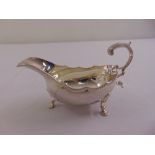 A silver sauce boat shaped oval with gadrooned border with leaf capped flying scroll handle on three
