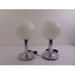 A pair of Art Deco style chrome and glass table lamps on circular bases with spherical glass shades
