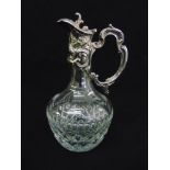 A continental white metal and cut glass claret jug with floral and leaf chased mount, double