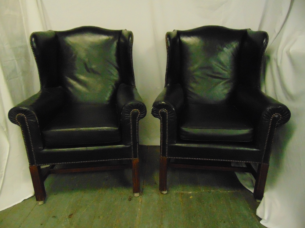 A pair of black leather armchairs on fluted rectangular mahogany legs