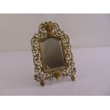 A late Victorian shaped rectangular table mirror in scroll pierced brass frame with hinged strut