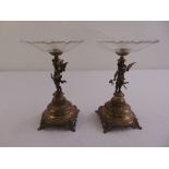 A pair of gilded metal and glass fruit stands with putti figurines supporting glass bowls on