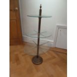 A brass and glass three tier stand with urn finial on raised circular base