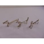 Three white metal knife rests in the form of stylised dogs