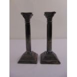 A pair of silver filled Corinthian column table candlesticks on stepped square bases with beaded