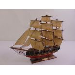 A wooden ships model of a three masted vessel with linen sails on raised rectangular plinth