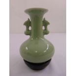 A Chinese celadon vase with pierced mask side handles on circular black stone plinth