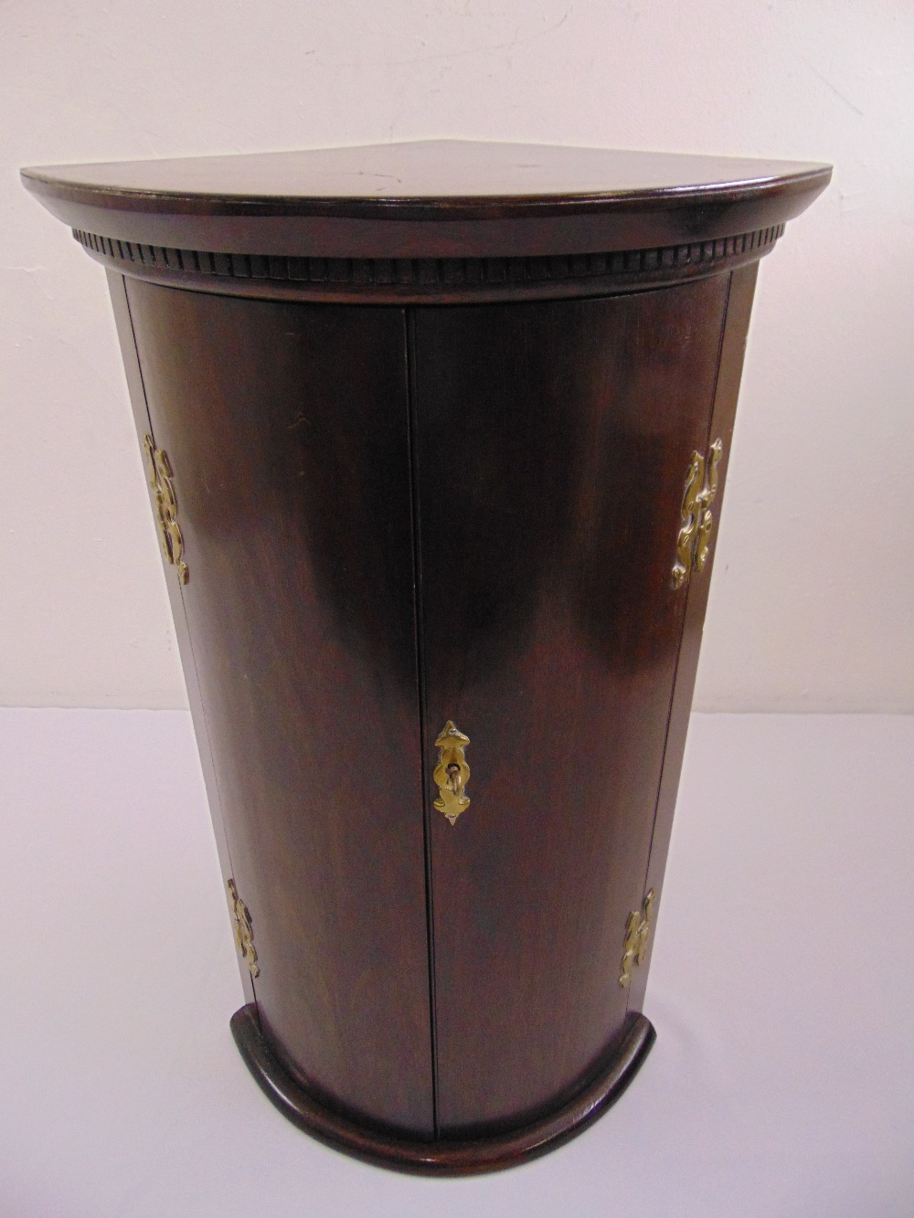 A mahogany wall hanging corner cabinet with brass hinges and escutcheon