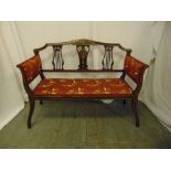 An Edwardian two seater settle with upholstered seat and arms, pierced slat inlaid back on four