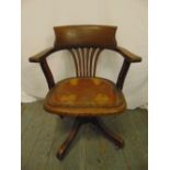 An early 20th century oak captains chair with leather seat and original castors, label to base A M