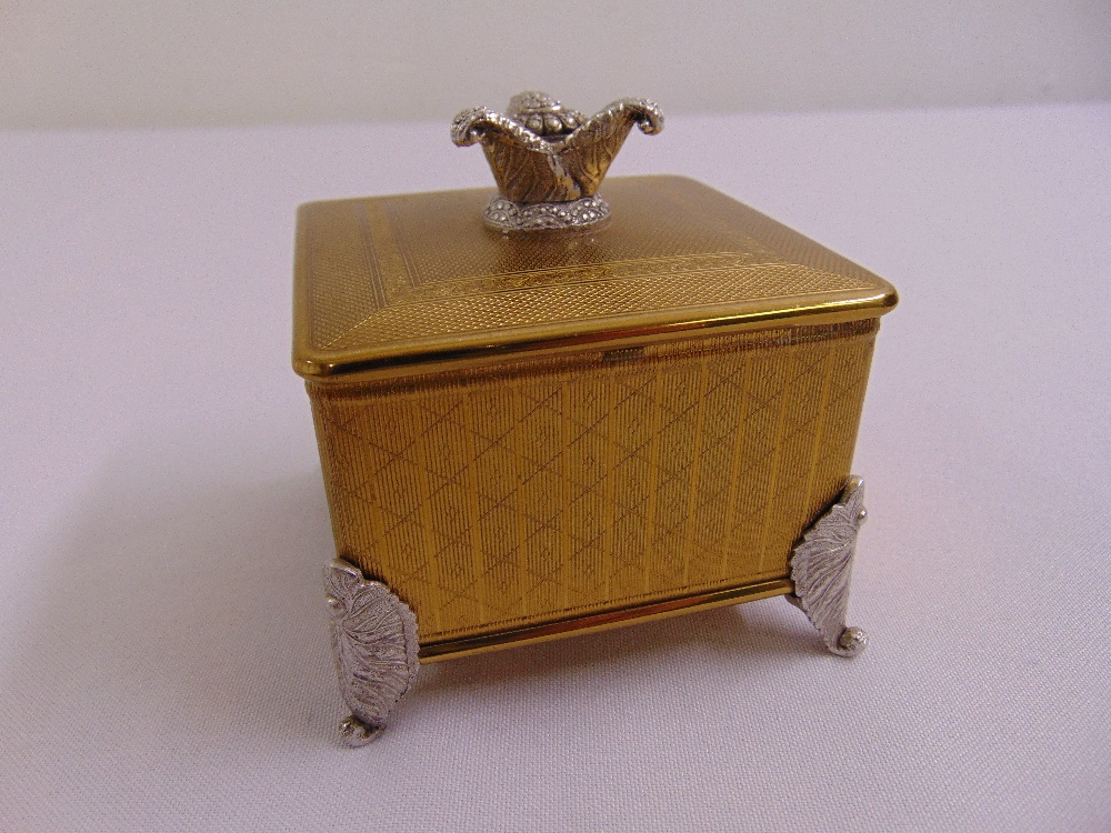 An engine turned gilded metal musical jewellery box with mirrored hinged cover on four leaf