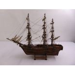 A wooden three masted model of a galleon with rigging and linen sails on raised wooden stand