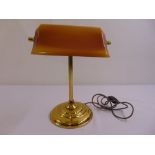 A brass desk lamp on raised circular base with integrated glass shade