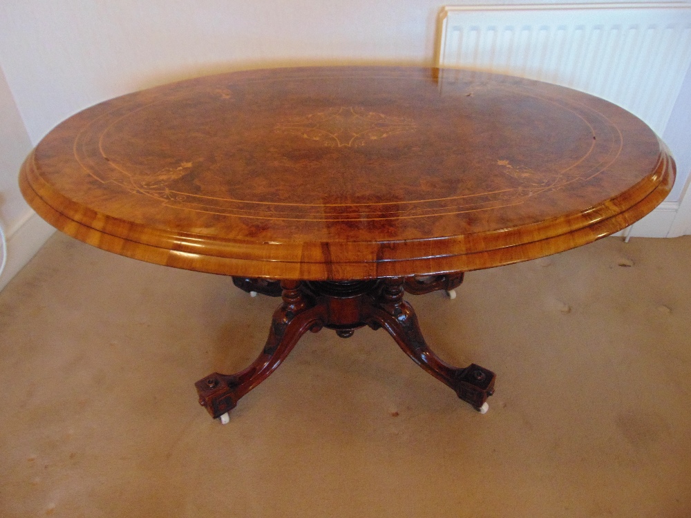 A Victorian oval inlaid walnut tilt top hall table on four outswept legs with original casters