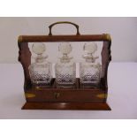 A brass bound oak Tantalus with three cut glass decanters with drop stoppers