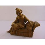 A French gilded metal figurine of a lady seated on a chaise longue