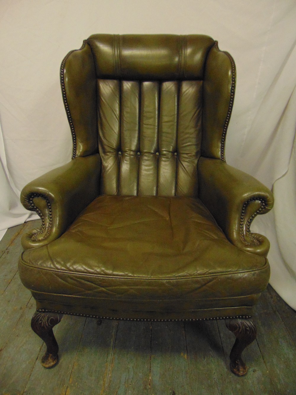 A green leather armchair, button back on scroll legs