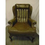 A green leather armchair, button back on scroll legs