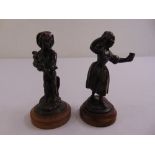 A pair of bronze figurines of a country boy and girl on raised circular plinths, one A/F