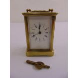 A brass carriage clock of customary form with white enamel dial and Roman numerals