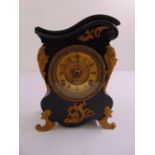 An antique mantle clock with black and gilt mounts with Roman numerals on scroll supports