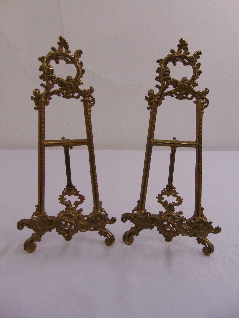 A pair of gilded metal scroll pierced table top picture easels with hinged struts