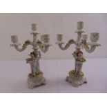 A pair of continental porcelain candelabra, supported by putti on raised pierced bases