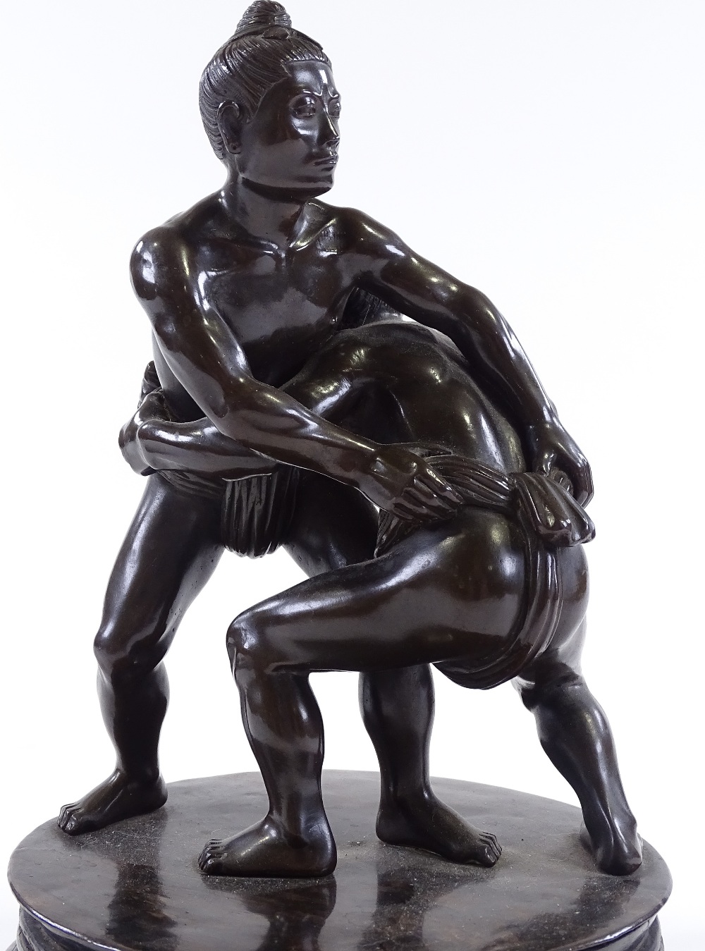 A Japanese bronze Sumo wrestling sculpture, early 20th century, unsigned, on circular ebony stand,