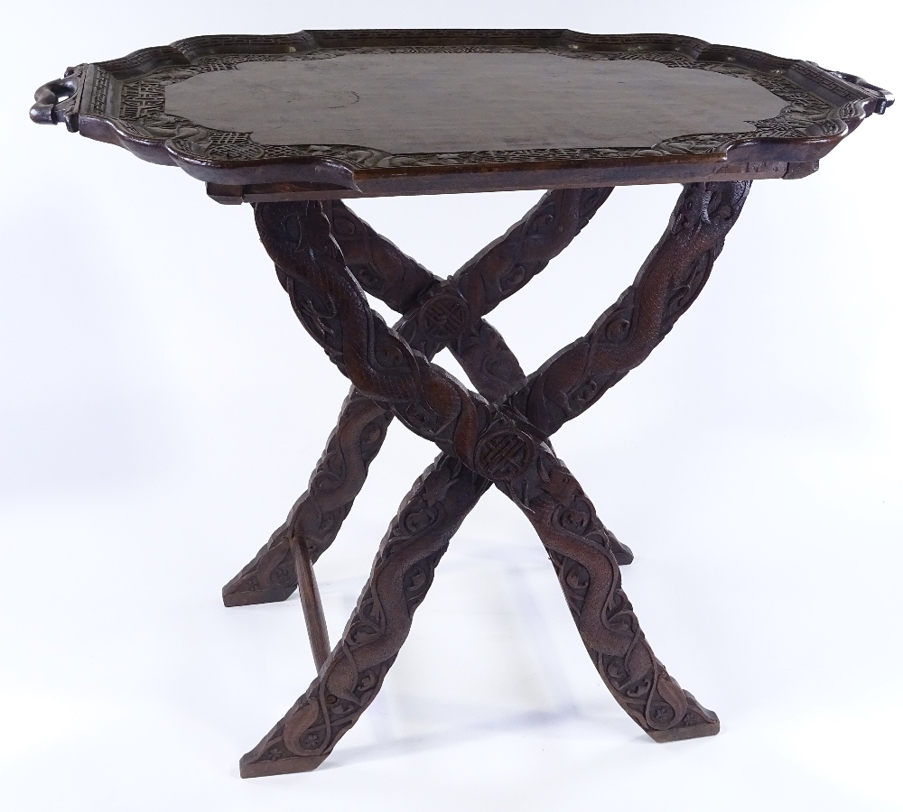 A Chinese hardwood 2-handled tea tray on folding stand, with relief carved dragon and symbolic