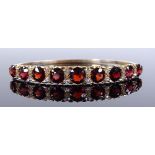 An unmarked gold graduated garnet and diamond hinged bangle, setting height 7.9mm, internal diameter