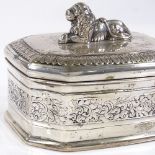 An octagonal white metal hinged box, with cast reclining lion finial and engraved foliate border,