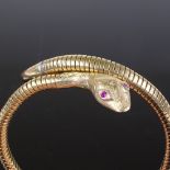 A 9ct gold snake bangle, with ruby eyes and textured engraved head, coiled gold body with steel