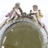 A Continental porcelain-framed oval mirror, surmounted by 2 cherubs, overall height 33cm