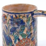 A glazed terracotta tankard with hand painted stylised floral design, height 13.5cm