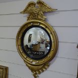 A gilt-framed convex wall mirror with ball mounts, surmounted by a carved giltwood eagle, height 3'