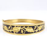 A Middle Eastern unmarked gold and black enamel hinged bangle, with engraved leaf decoration, band