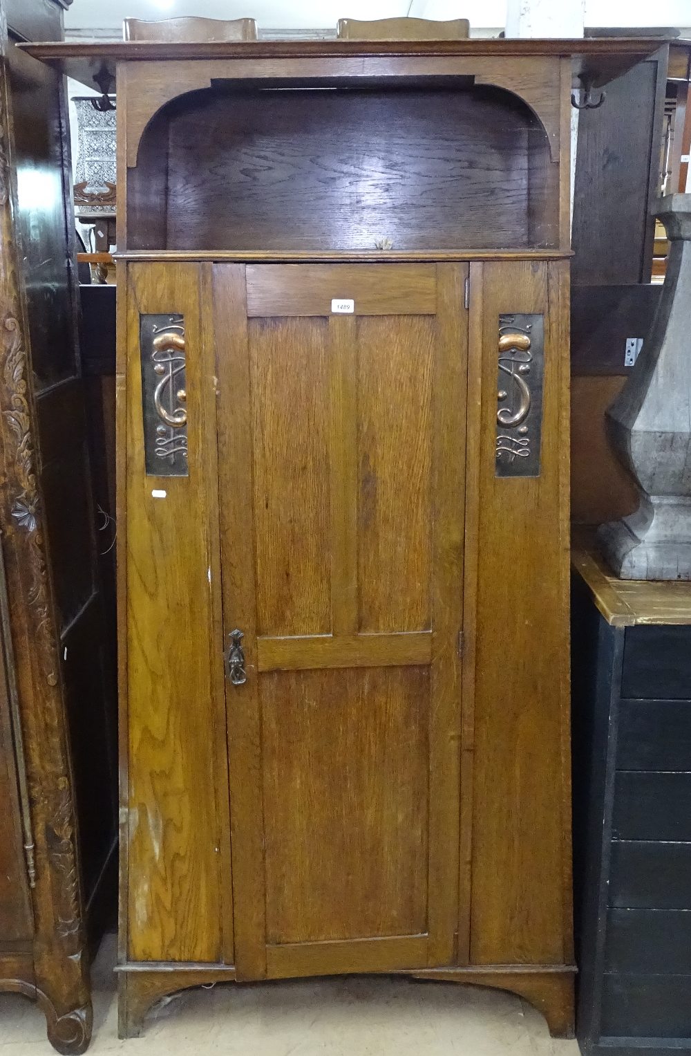 A stylised Art Nouveau oak hall cupboard, with single panel door and copper panels, on bracket feet,