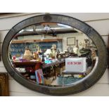 An Antique oval hammered-metal framed bevelled-edge wall mirror, length 80cm