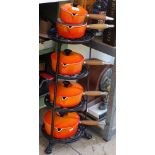 A graduated set of 5 Le Creuset orange pans with wooden handles, and pan stand