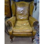 A distressed leather upholstered wing armchair, raised on acanthus leaf carved cabriole legs.