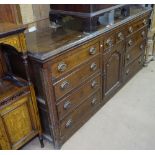 An 18th century oak dresser base, with 10 fitted drawers, and arch panelled cupboard door to the