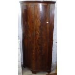 A large cross-banded mahogany floor standing bow-front corner cupboard, with 2 panelled doors,
