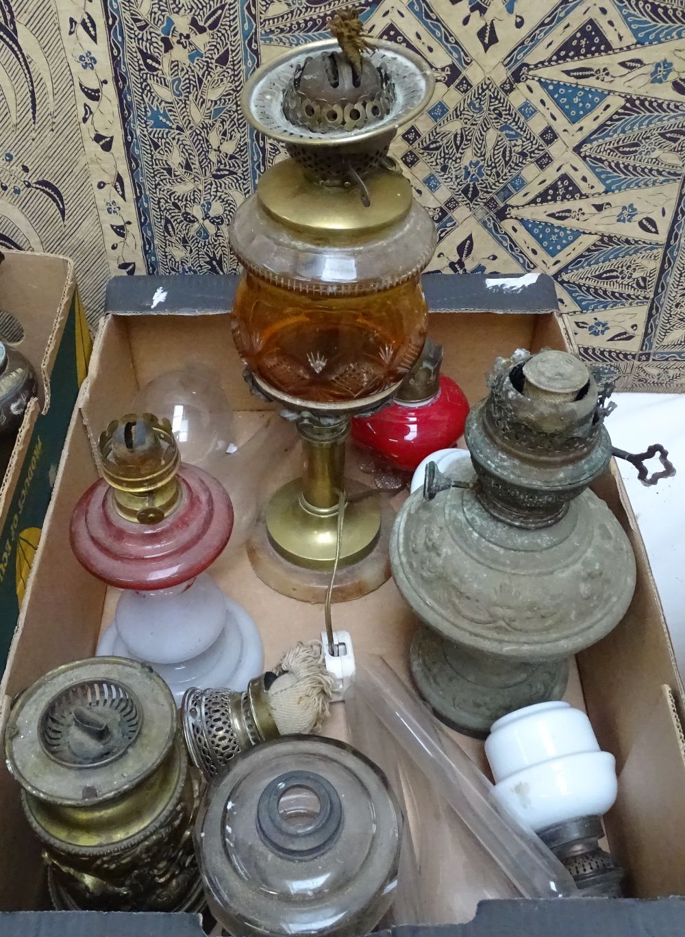 A brass oil lamp with amber glass font, and other oil lamps and chimneys