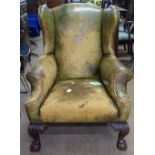 A distressed leather upholstered wing armchair, raised on acanthus leaf carved cabriole legs, with
