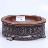 A copper dish set in a cast-metal Eastern stand with script, 17cm across