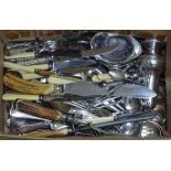 A box containing plated cutlery, a sauce boat, silver sugar tongs, teaspoon etc