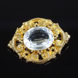 An unmarked gold large oval aquamarine brooch, in pierced and engraved foliate scroll surround,